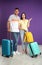 Couple with suitcases for summer trip near purple wall. Vacation travel