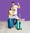 Couple with suitcases and tickets in passports for summer trip near purple wall. Vacation travel