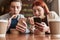 A couple of teenagers totally absorbed in using their phones, ignoring each other while sitting in a cafe together on a