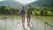 A couple of tourists walk with caution over a unsteady bridge over a mountain river. Rear view, steadicam shot