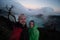 Couple travelers standing on edge of crater Ijen volcano with colorful sky at morning