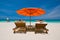 Couple on a tropical beach on deck chairs under a red umbrella