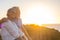 Couple of two cute seniors together enjoying summer and having fun at the beach looking at the sea or ocean with sunset - mature