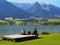 Couple with two dogs sits on jetty with a lake and mountains in the background, Walchsee, Austria