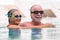 Couple of two seniors and mature people together in the pool swimming and having fun hugged - active and fitness lifestyle and