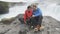 Couple Using Smartphone At Godafoss Waterfall - Tourist Destination Iceland