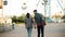 Couple walking in amusement park. Hipster man and stylish woman go to ride on ferris wheel. Boyfriend and girlfriend