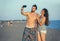 Couple walking on beach at sunset taking selfie picture on mobil