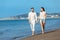 Couple walking on beach. Young happy interracial couple walking on beach smiling holding around each other.
