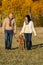 Couple walking dog in autumn sunny park