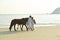 A couple walking horses on beach