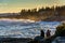 Couple watching large waves crash on rocks at sunset, at Pemaquid Point, Maine.