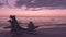 Couple watching romantic beach sunset - Lovers enjoying watching sunset on summer travel destination sitting on tree