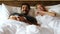 Couple watching television together on cozy bed on weekend holiday. Handsome husband and beautiful wife love to stay together and