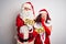 Couple wearing Santa costume holding wow and sale banner over isolated white background hand on mouth telling secret rumor,