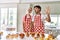 Couple of wife and husband cooking pastries at the kitchen showing and pointing up with fingers number five while smiling