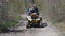 A couple on a yellow quad bike riding on a dirt road in the spring forest. Front view. Extreme type of outdoor