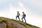 Couple of Young Happy Travelers Hiking with Backpacks on the Rocky Trail at the Evening. Family Travel and Adventure