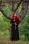 Courageous young lady with long red hair in image of fabulous historical character of witch and priestess in a mystical forest