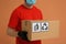 Courier holding cardboard box with packaging symbols on orange background, closeup. Parcel delivery