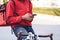 Courier in red uniform with a delivery box on back riding a bicycle and looking on the cellphone to check the address to deliver