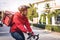 Courier in red uniform with a delivery box on back riding a bicycle and looking on the cellphone to check the address to deliver