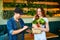 Courier service worker delivering fresh food, giving shopping bag to a happy woman client on the kitchen at home. Online grocery