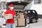 Courier in uniform, protective mask and gloves stands near trunk of car with parcels