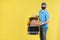 Courier wearing virus protection mask and medical food delivery gloves with yellow open thermos bag holds out an order