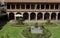 A courtyard with flower gardens surrounded by two story stone walls lined with columns and arches at the Belmond Monasterio Hotel