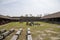 The courtyard of a military fort with brown wooden pergolas, brown wooden tables and benches and tools and equipment on the grass