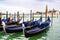 Covered gondolas docked on water between wooden mooring poles in Venice, Italy. Church of San Giorgio Maggiore in background.