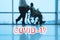 COVID-19 billboard red text on blue medical hospital background with doctor walking with disabled patient in wheelchair