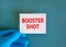 Covid-19 booster shot vaccine symbol. White note with words booster shot, beautiful blue background, doctor hand in blue glove.