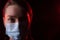 Covid-19 epidemic. Coronavirus pandemic. Sad infected woman in a protective medical mask with headache and fever on a dark red