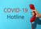Covid-19 Hotline. Woman with red handset and text on blue background, closeup