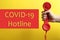 Covid-19 Hotline. Woman with red handset and text on yellow background, closeup