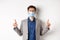 Covid-19, pandemic and business concept. Suspicious businessman in medical mask pointing up and thinking, having doubts