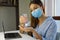 COVID-19 Pandemic Coronavirus Woman with Surgical Mask Working from Home using Alcohol Gel from Dispenser, against 2019-nCoV. Home