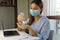 COVID-19 Pandemic Coronavirus Woman with Surgical Mask Working from Home using Alcohol Gel from Dispenser, against 2019-nCoV. Home