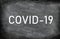 COVID-19 white chalck text on blackboard chalkboard texture distressed grunge background. Graphic design of corona virus