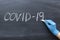 Covid-19 word written on a blackboard. Hand with chalk in a medical glove