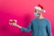 Covid christmas concept. young man with santa claus hat and face mask and gifts in studio with red background, happy smiling face