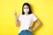 Covid, health care and pandemic concept. Asian female model in medical mask and white t-shirt pointing finger at upper
