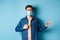 Covid and healthcare concept. Handsome modern guy in medical mask pointing at empty space aside, standing on blue