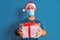 Covid19 christmas concept. young man with santa claus hat and face mask and gifts in studio with colorful blue background, happy