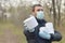 Covidiot concept. Young man in protective mask holds many rolls of toilet paper outdoors in spring wood