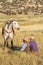 Cowboy and Cowgirl Sitting in Grass Holding Horse