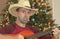 A Cowboy with a Guitar by a Christmas Tree