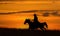 Cowboy on horseback gallops against dawn sky